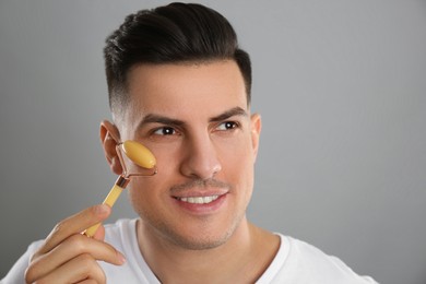 Photo of Man using mineral facial roller on grey background. Space for text