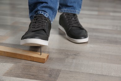 Photo of Careless man stepping on nail in wooden plank, closeup