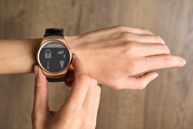 Young woman checking electronic wristwatch with Smart Home Interface on wooden background, closeup