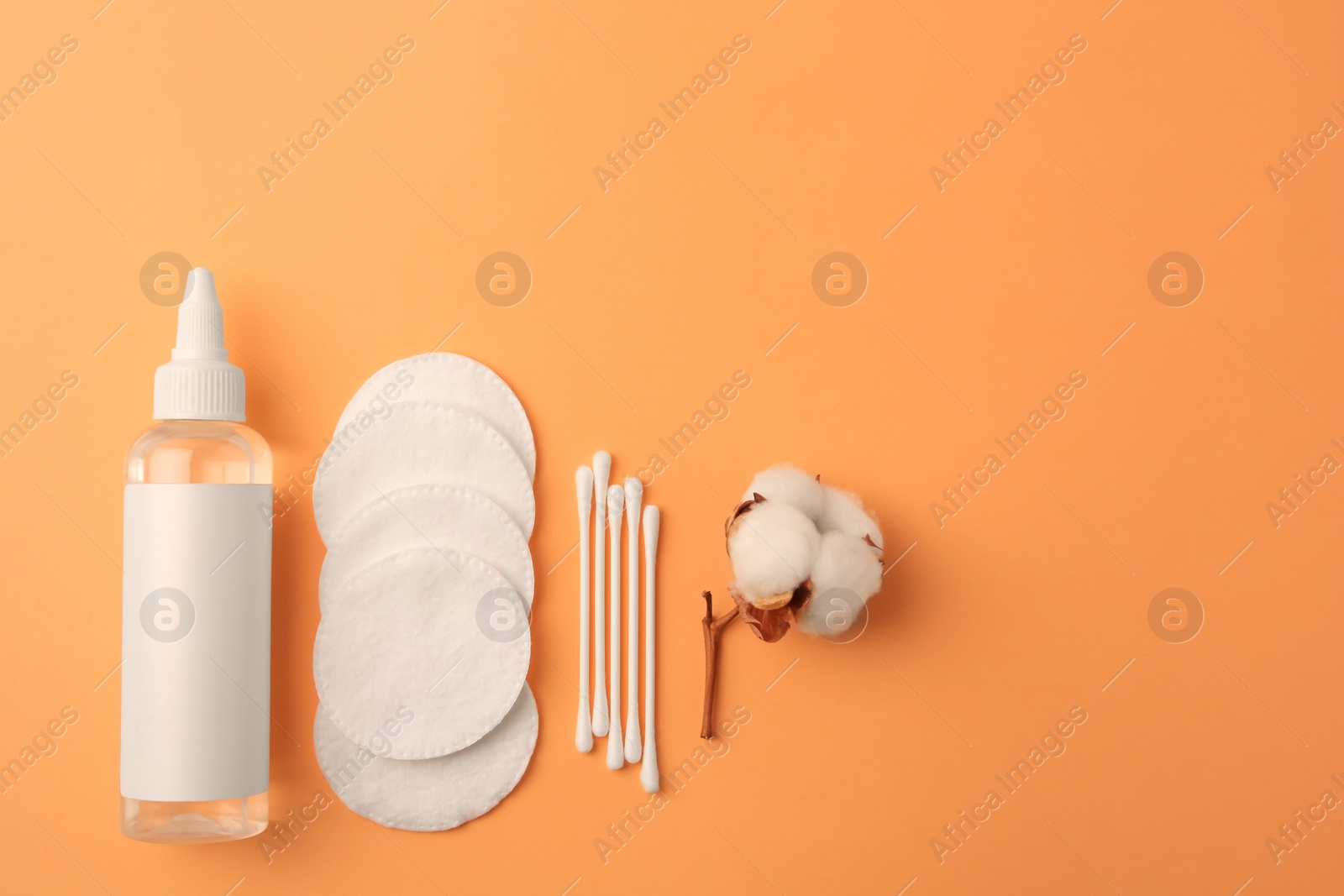 Photo of Flat lay composition with makeup remover and cotton flower on pale orange background, space for text