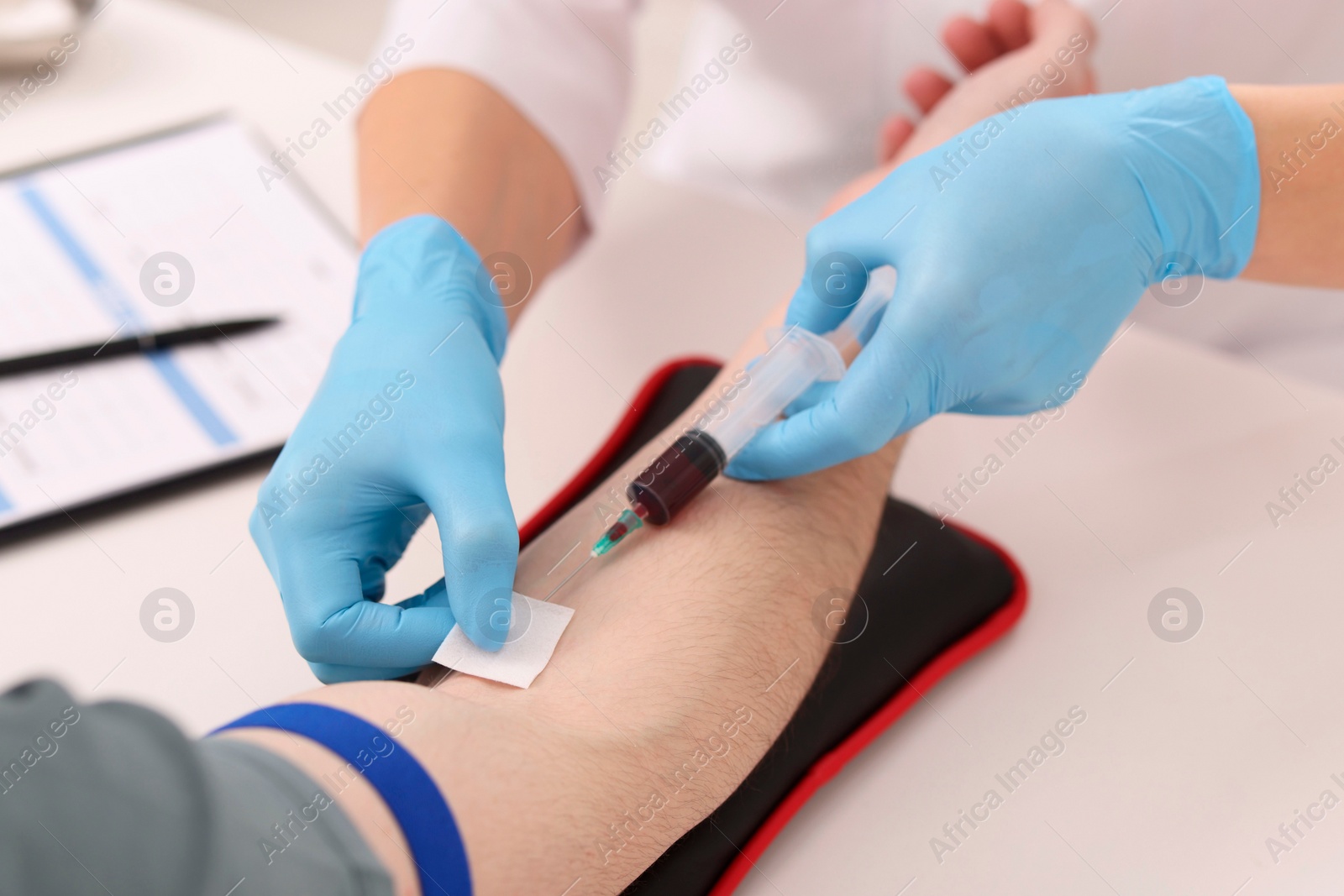 Photo of Doctor taking blood sample from patient with syringe at white table in hospital, closeup