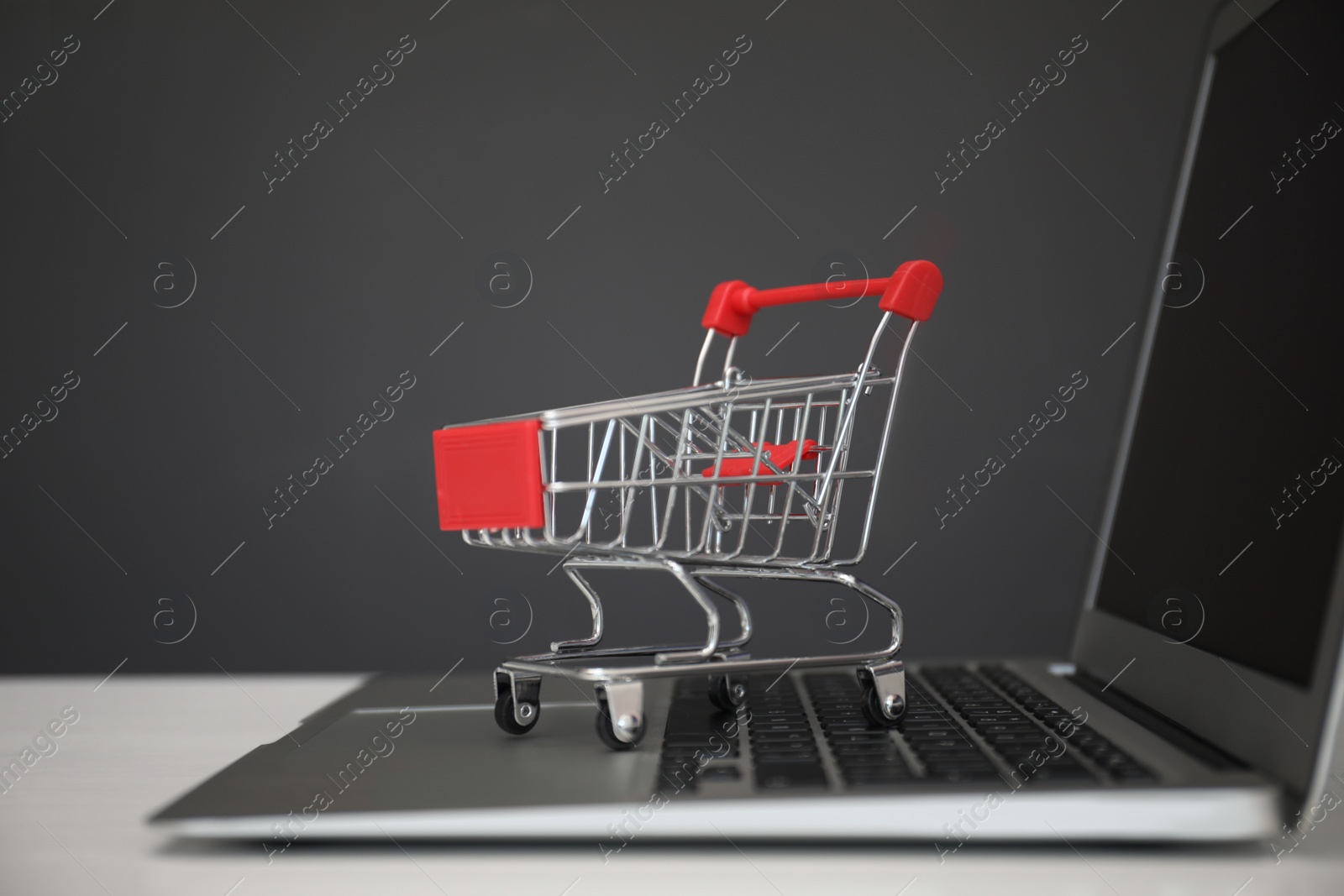 Photo of Internet shopping. Laptop with small cart on table against grey background