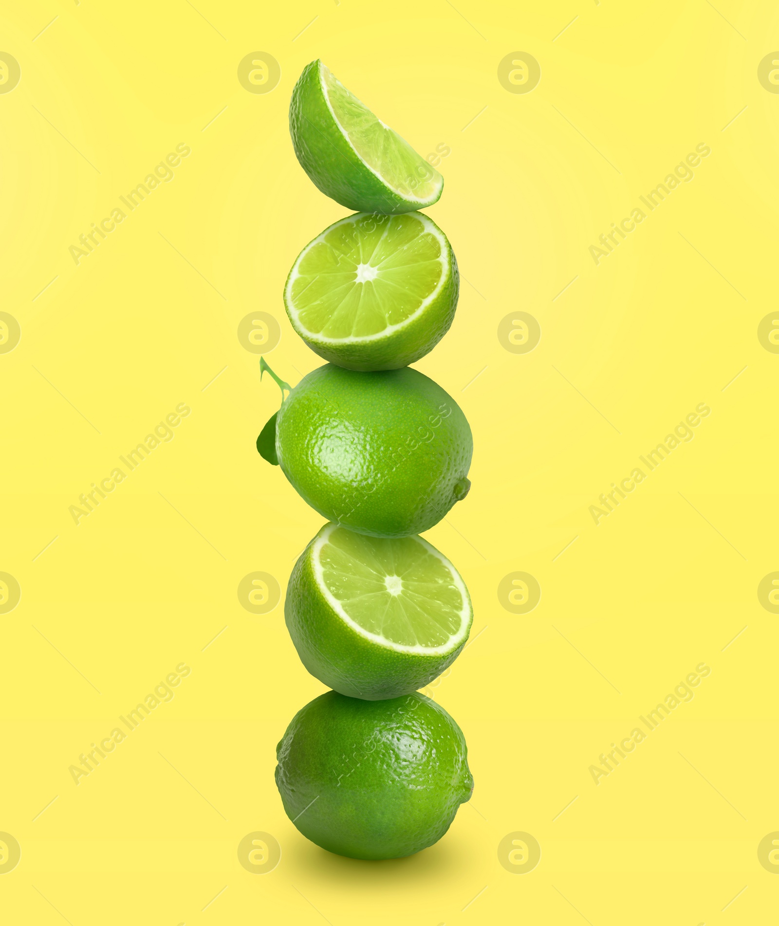 Image of Stacked whole and cut limes on yellow background