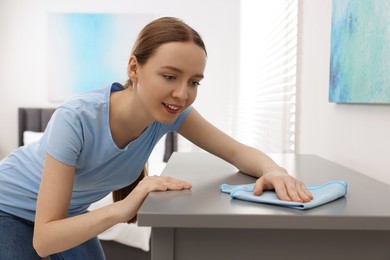 Photo of Woman with microfiber cloth cleaning grey chest of drawers in room