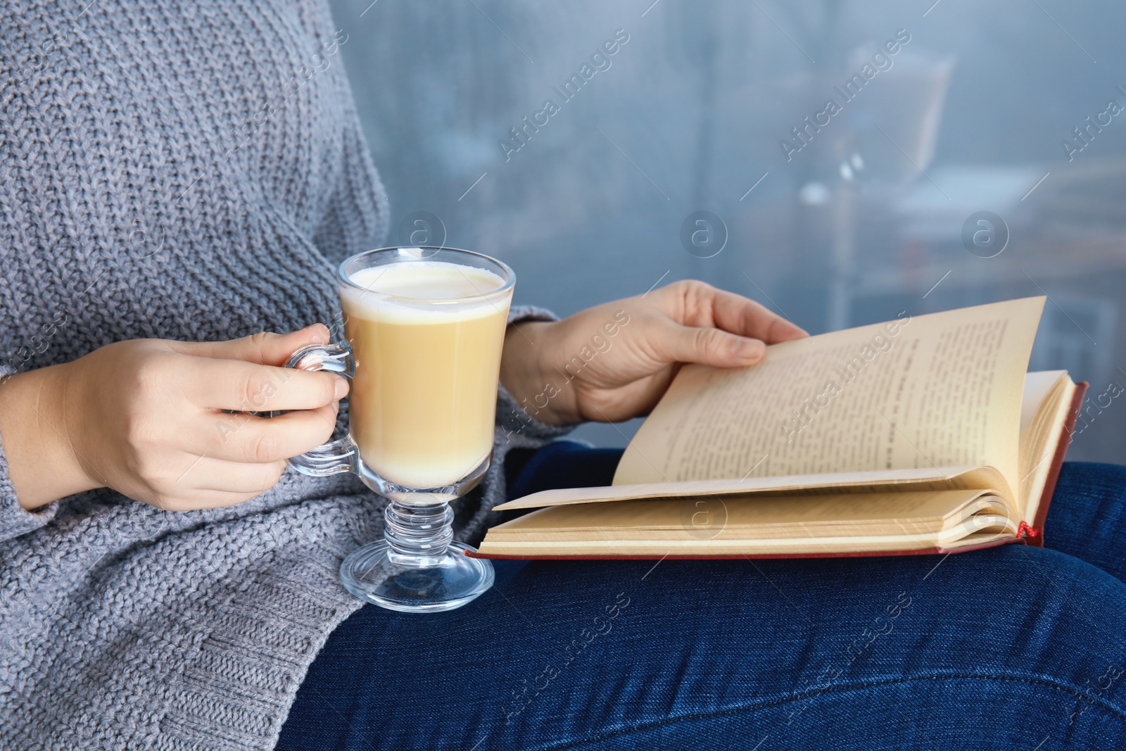 Photo of Woman with cup of coffee reading book at home, closeup