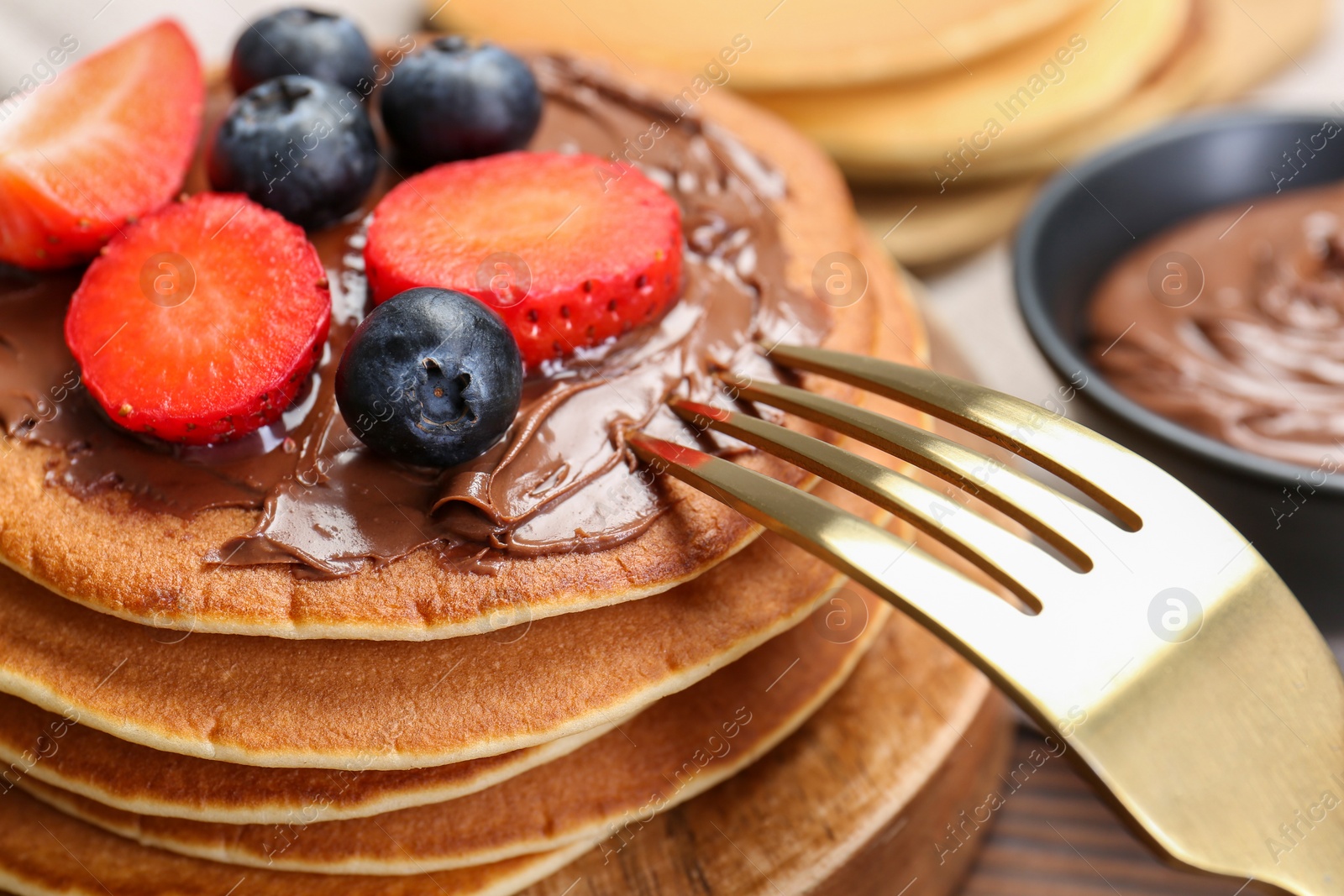 Photo of Tasty pancakes with chocolate paste, berries and fork on wooden table, closeup