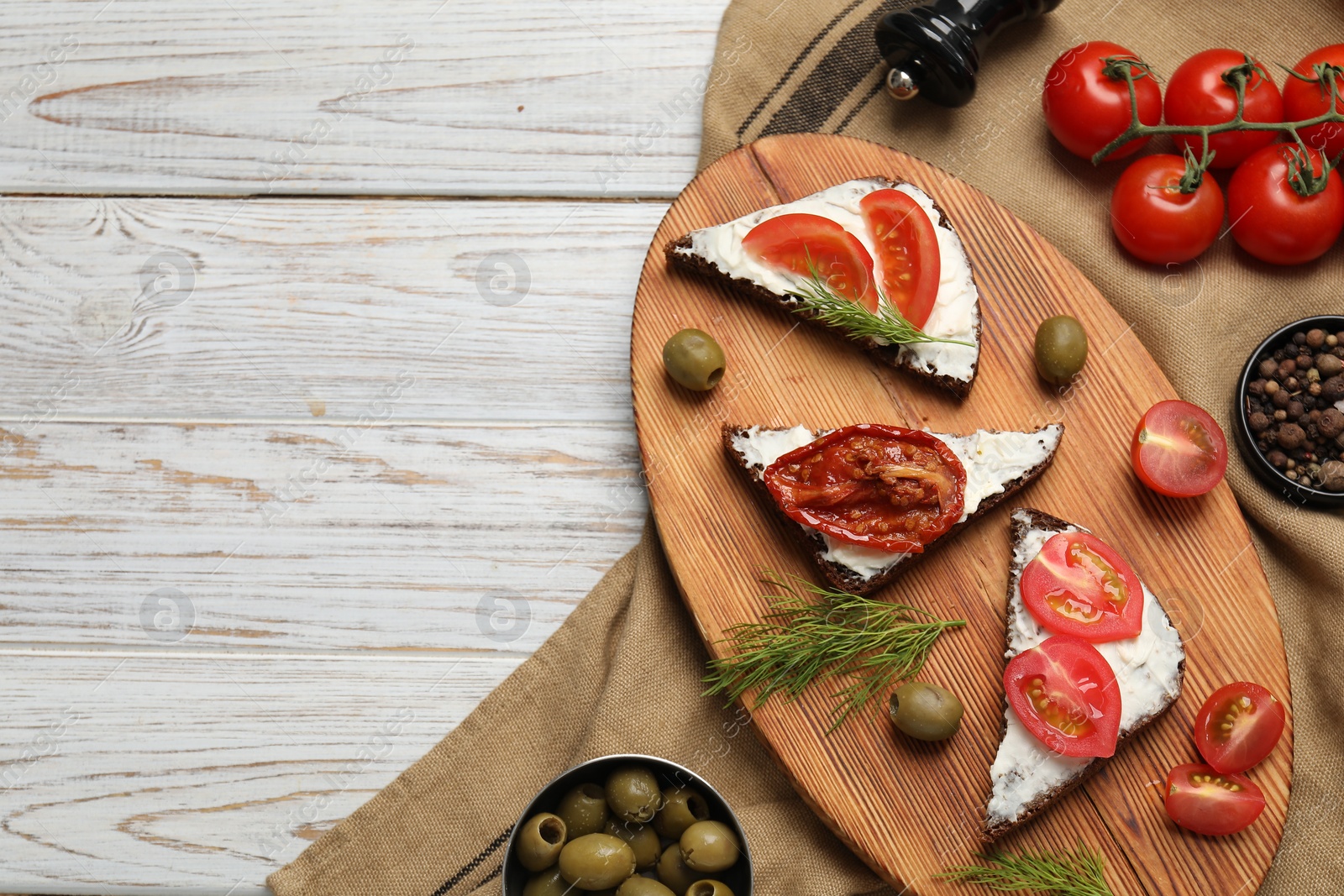 Photo of Delicious bruschettas with ricotta cheese, dill, olives, fresh and sun dried tomatoes on light wooden table, top view. Space for text