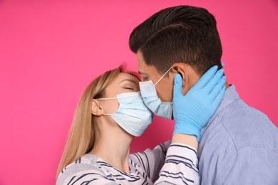 Couple in medical masks and gloves trying to kiss on pink background