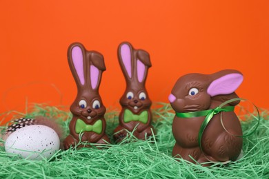 Photo of Easter celebration. Funny chocolate bunnies and painted egg with feather on grass against red background