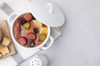 Photo of Meat solyanka soup with thin dry smoked sausages in pot on light table, flat lay. Space for text