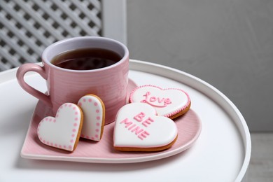 Delicious heart shaped cookies and cup of tea on white table