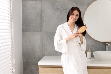 Beautiful woman brushing her hair near mirror in bathroom, space for text