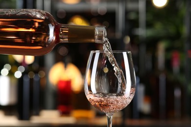 Photo of Pouring rose wine from bottle into glass on blurred background, closeup