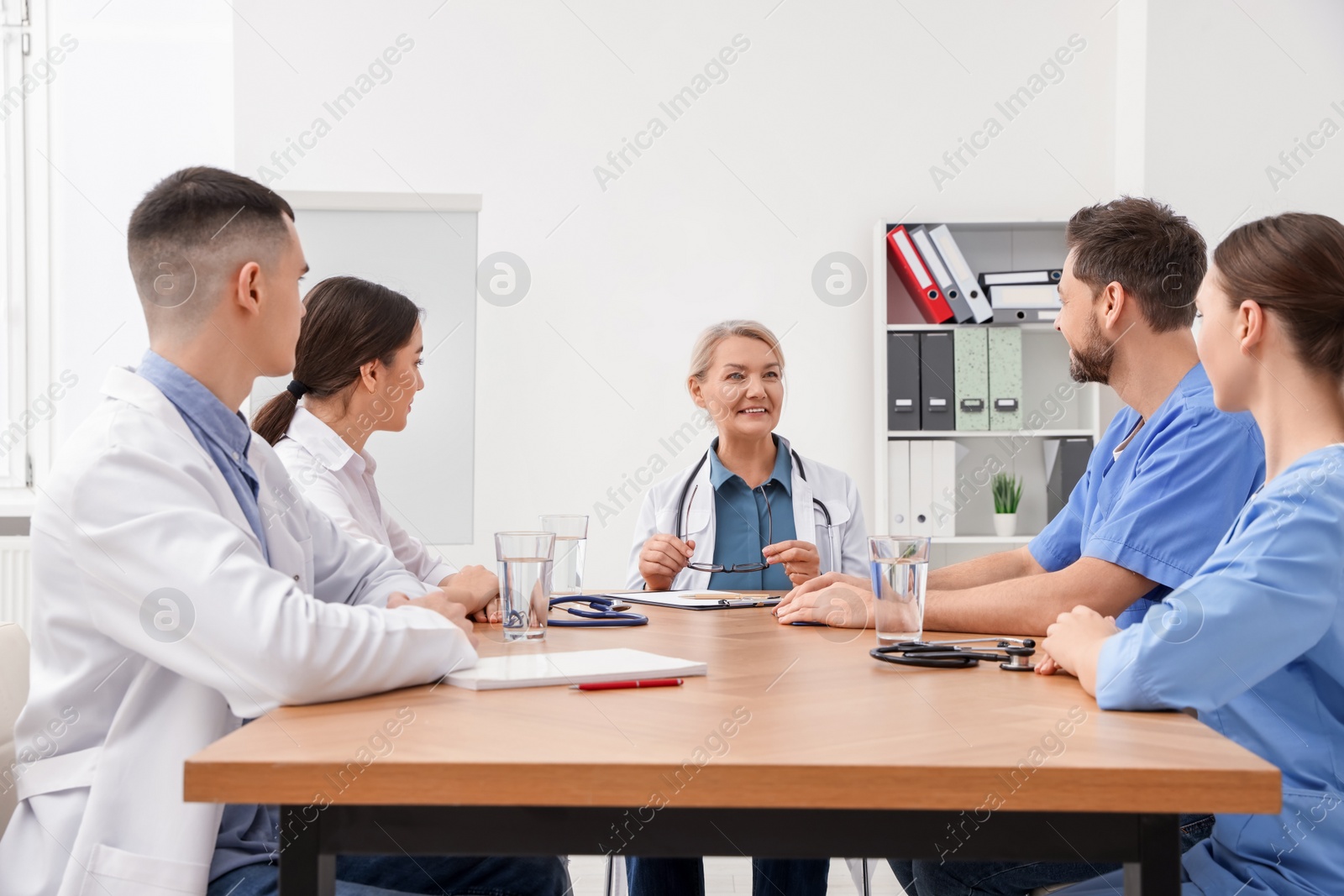 Photo of Medical conference. Team of doctors listening to speaker at wooden table in clinic