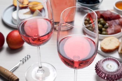Glasses of delicious rose wine and snacks on white table, closeup