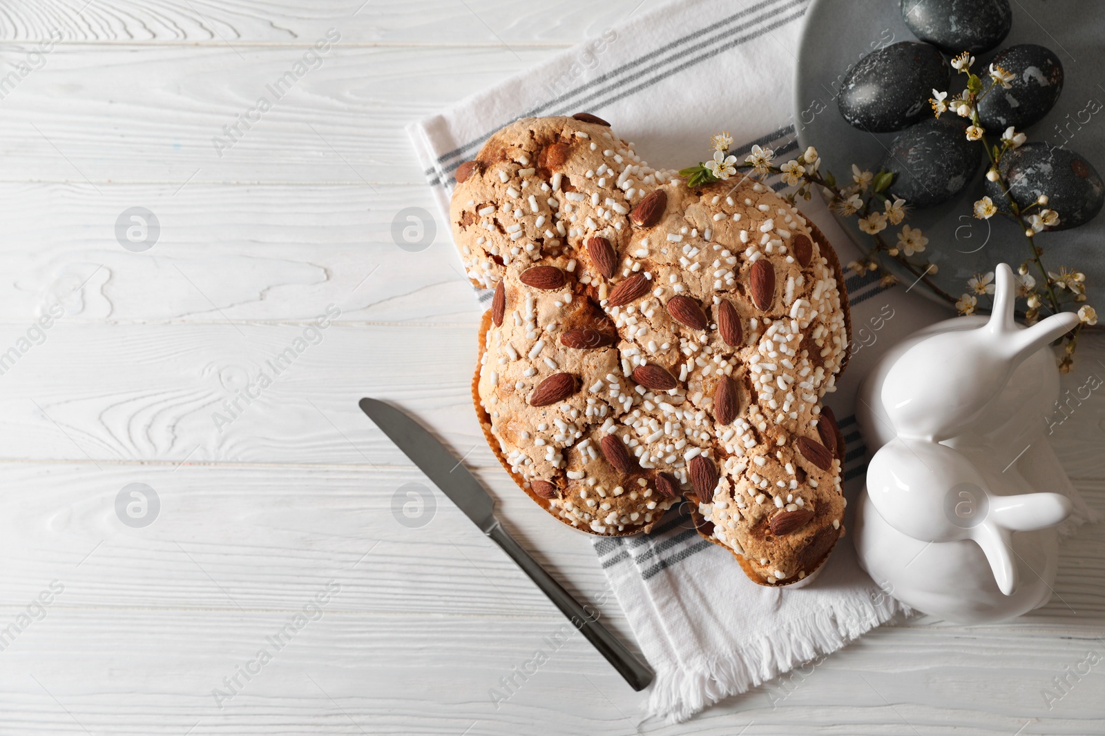 Photo of Delicious Italian Easter dove cake (Colomba di Pasqua), decorated eggs and bunny figures on white wooden table, flat lay. Space for text