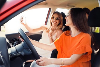 Happy beautiful young women taking selfie in car