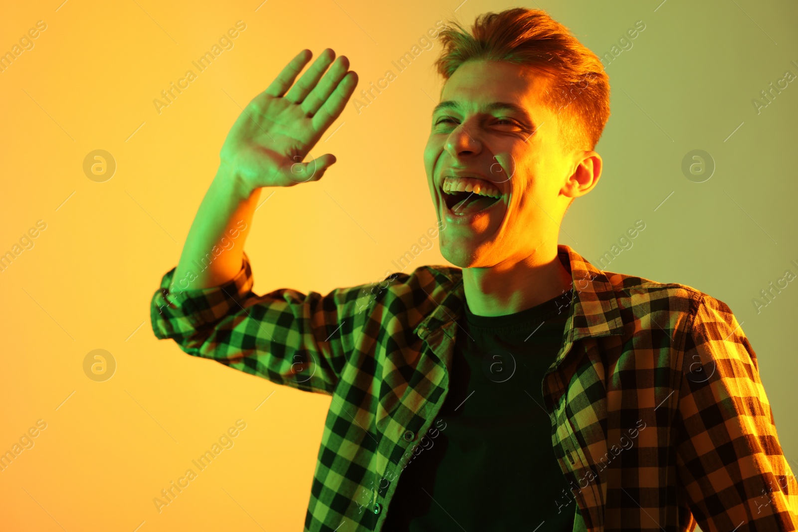 Photo of Young man greeting someone on color background in neon lights