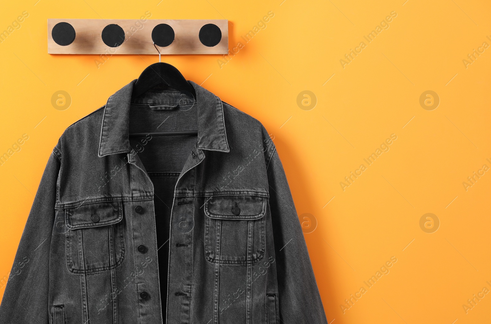 Photo of Hanger with dark gray denim jacket on orange wall, space for text