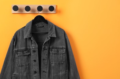 Photo of Hanger with dark gray denim jacket on orange wall, space for text