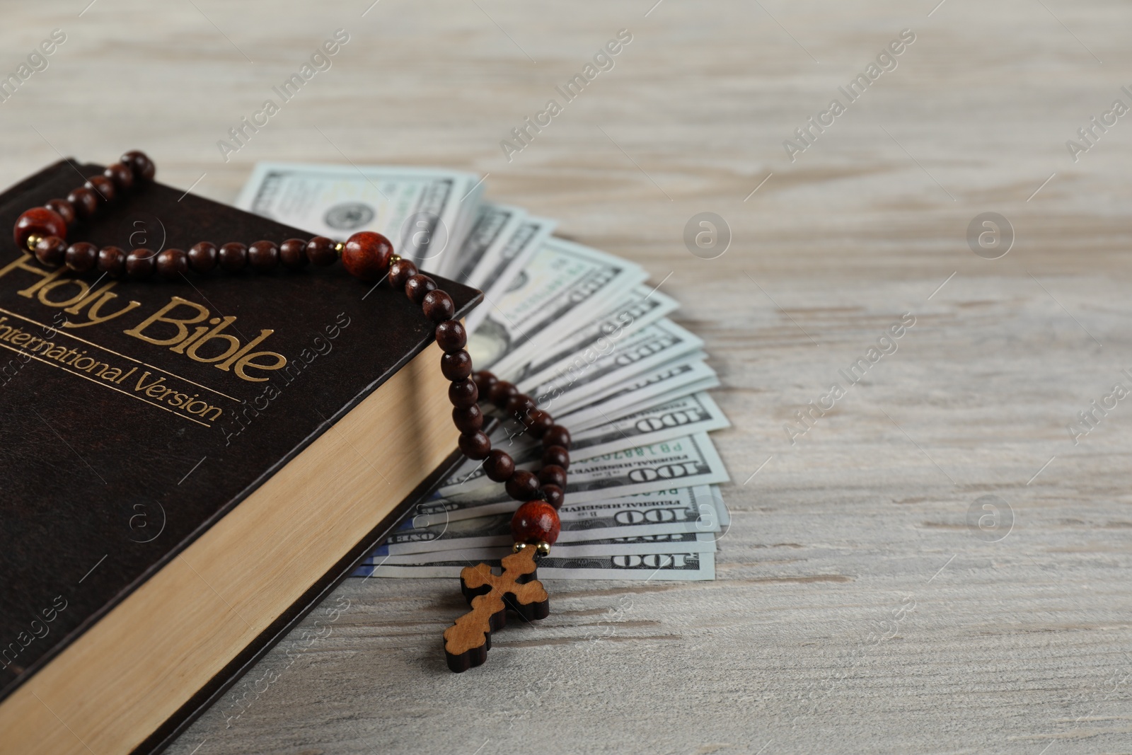 Photo of Holy Bible, cross and money on wooden table, closeup. Space for text