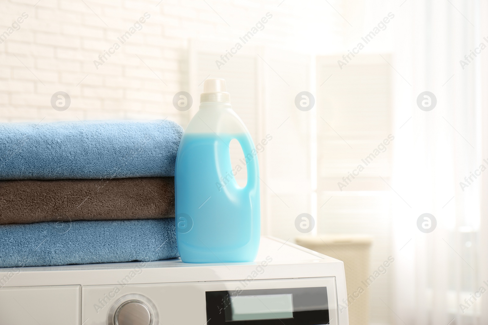 Photo of Bottle of detergent and clean towels on washing machine indoors, space for text. Laundry day