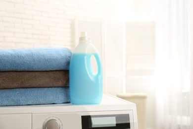 Bottle of detergent and clean towels on washing machine indoors, space for text. Laundry day