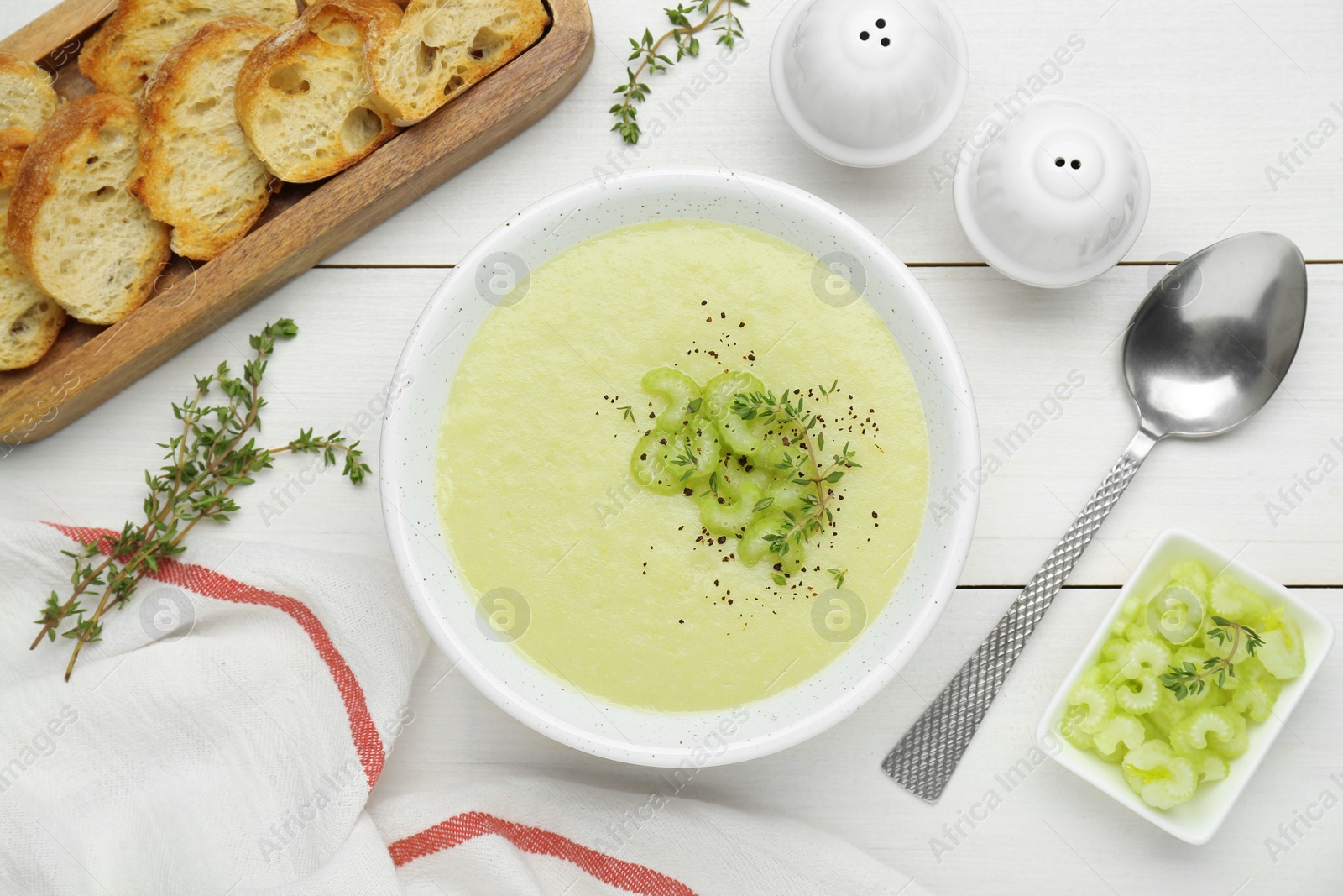Photo of Bowl of delicious celery soup served on white wooden table, flat lay