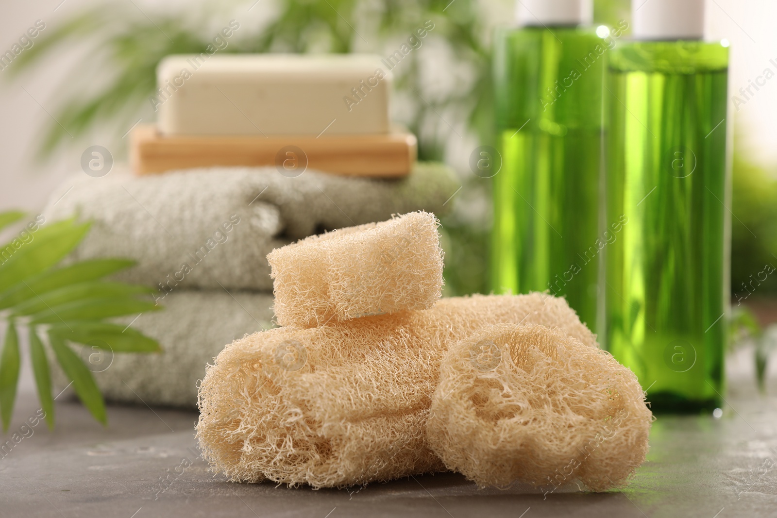 Photo of Loofah sponges, towels, soap, cosmetic products on grey table, selective focus