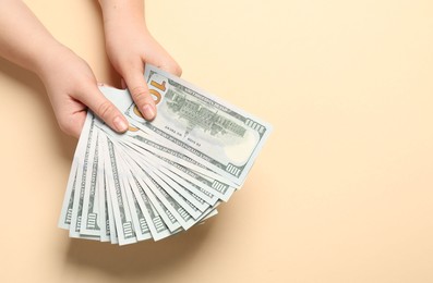 Money exchange. Woman holding dollar banknotes on beige background, top view. Space for text