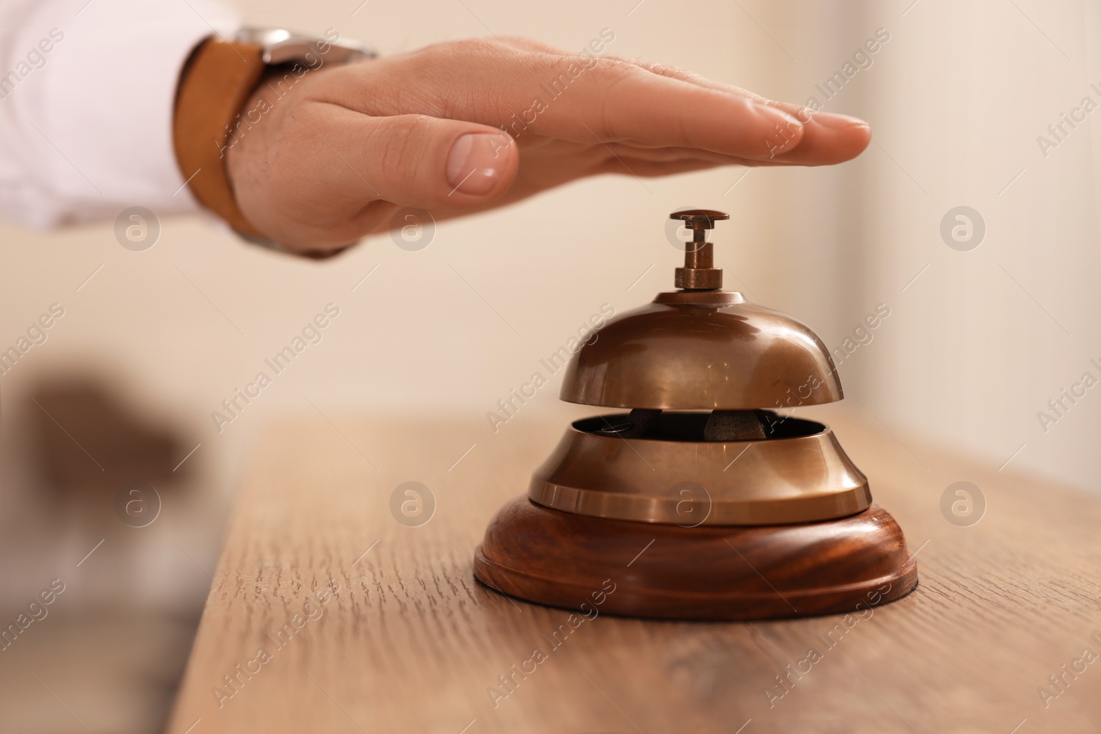 Photo of Man ringing service bell at wooden reception desk in hotel, closeup