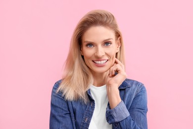 Photo of Portrait of smiling middle aged woman with blonde hair on pink background. Space for text