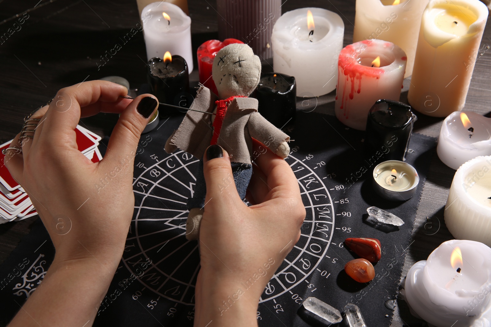 Photo of Woman stabbing voodoo doll with needle at table, closeup. Curse ceremony