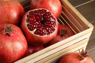 Photo of Ripe pomegranates in wooden crate on table, closeup