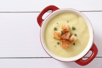 Photo of Tasty potato soup with croutons and rosemary in ceramic pot on white wooden table, top view. Space for text