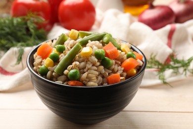 Delicious pearl barley with vegetables in bowl on wooden table, closeup