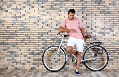 Photo of Handsome young hipster man with bicycle near brick wall