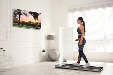 Image of Sporty woman training on walking treadmill and watching TV at home