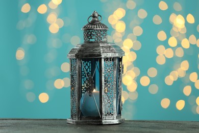 Photo of Traditional Arabic lantern on wooden table against light blue background with blurred lights