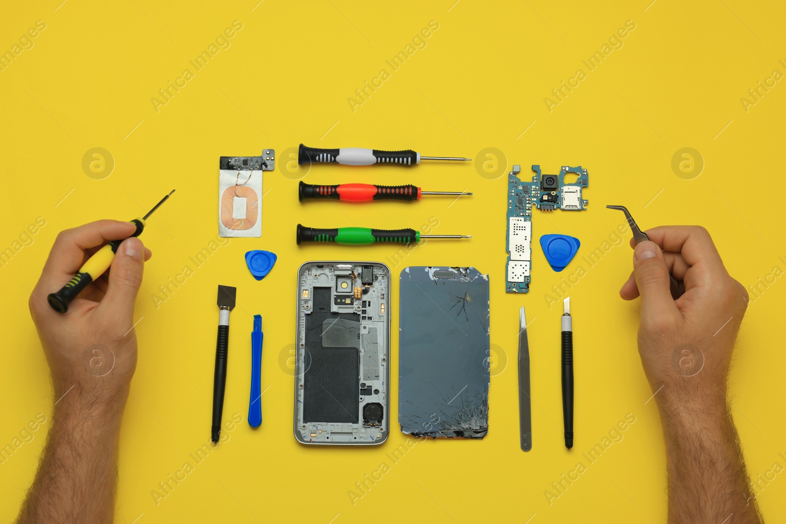 Photo of Man repairing broken smartphone on yellow background, top view