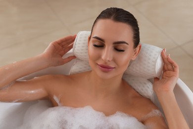 Photo of Young woman using pillow while enjoying bubble bath indoors