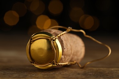 Photo of Cork of sparkling wine and muselet cap on wooden table against blurred festive lights, closeup. Bokeh effect