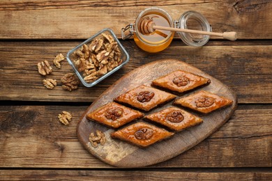 Photo of Delicious sweet baklava with walnuts and honey on wooden table, flat lay