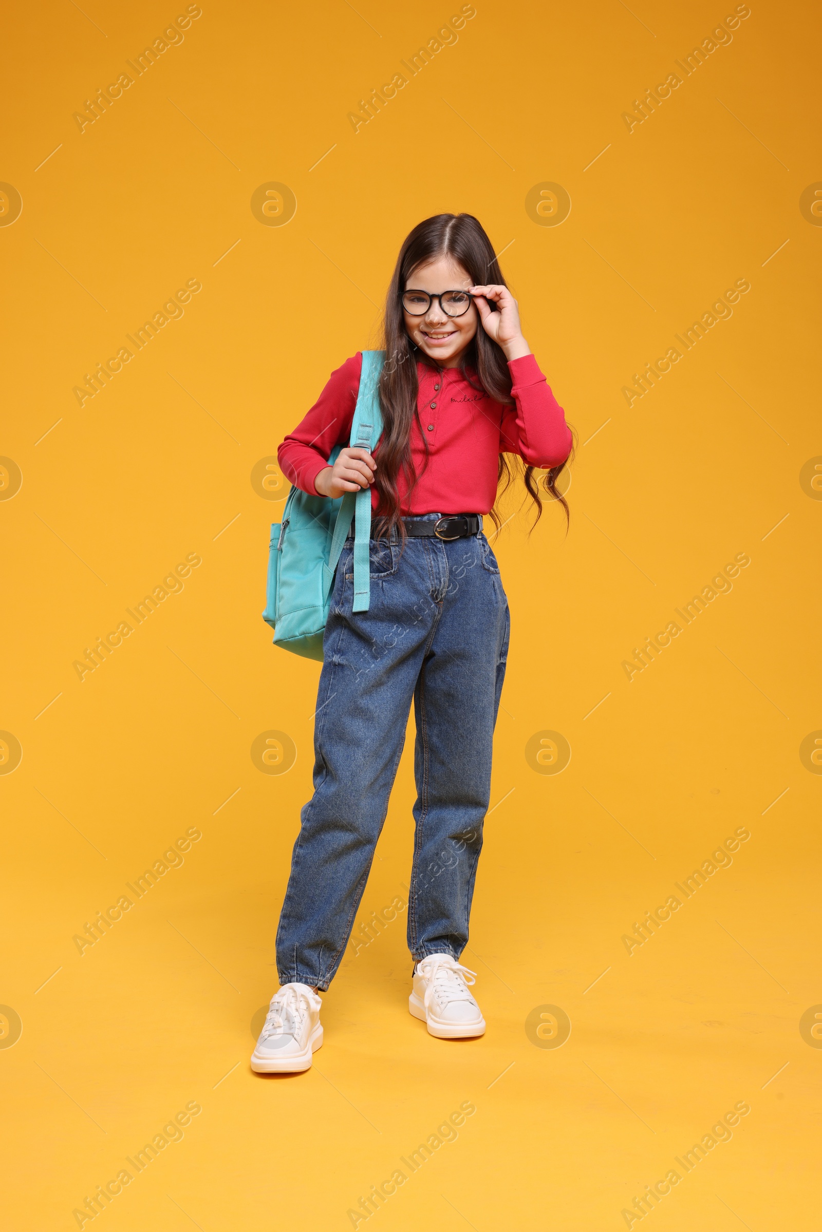 Photo of Cute schoolgirl in glasses on orange background