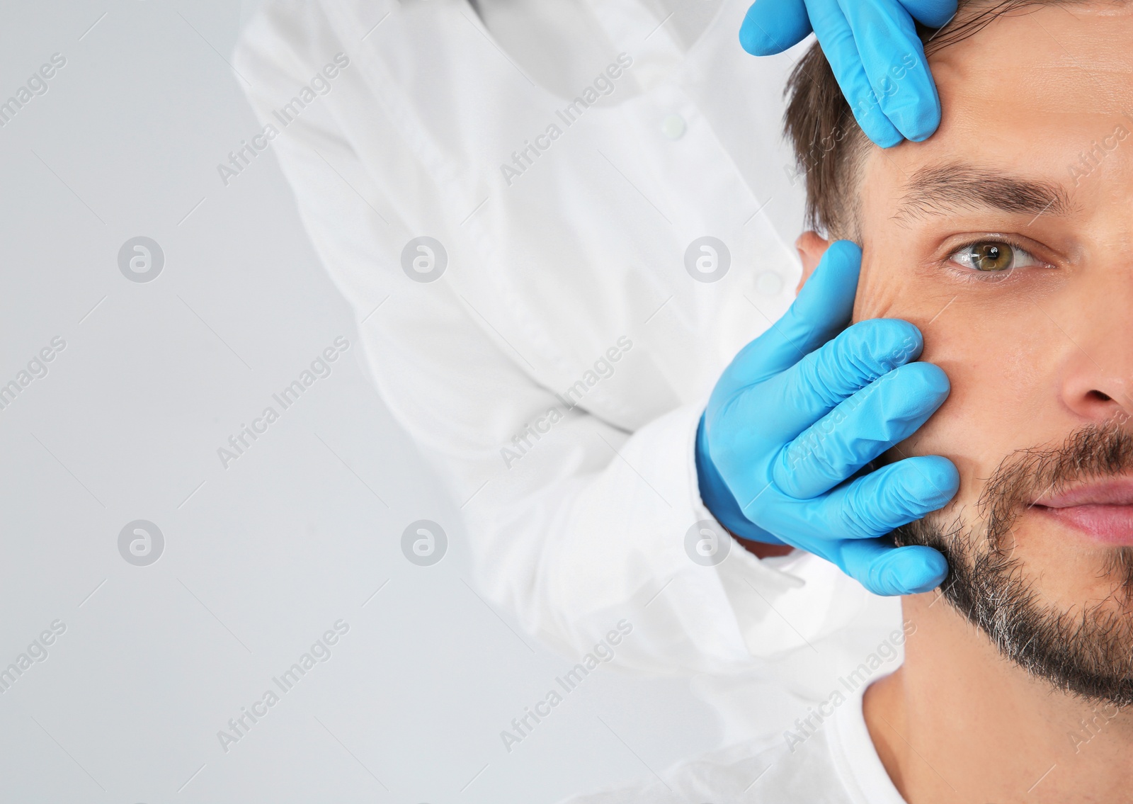 Photo of Doctor examining mature man face before cosmetic surgery on white background, closeup