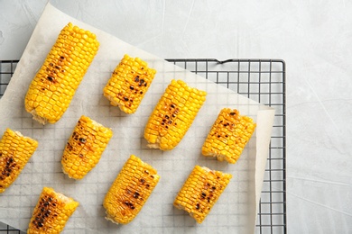 Cooling rack with grilled corn cobs on light background, top view