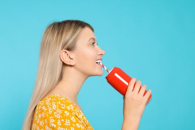 Beautiful happy woman drinking from red beverage can on light blue background