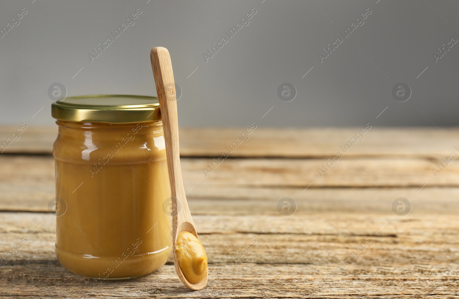 Photo of Jar and spoon with tasty mustard sauce on wooden table, space for text