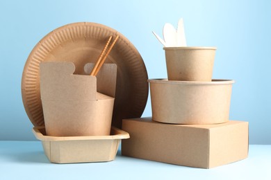 Photo of Eco friendly food packaging. Paper containers and tableware on white table against light blue background