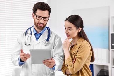 Photo of Doctor with tablet consulting patient during appointment in clinic